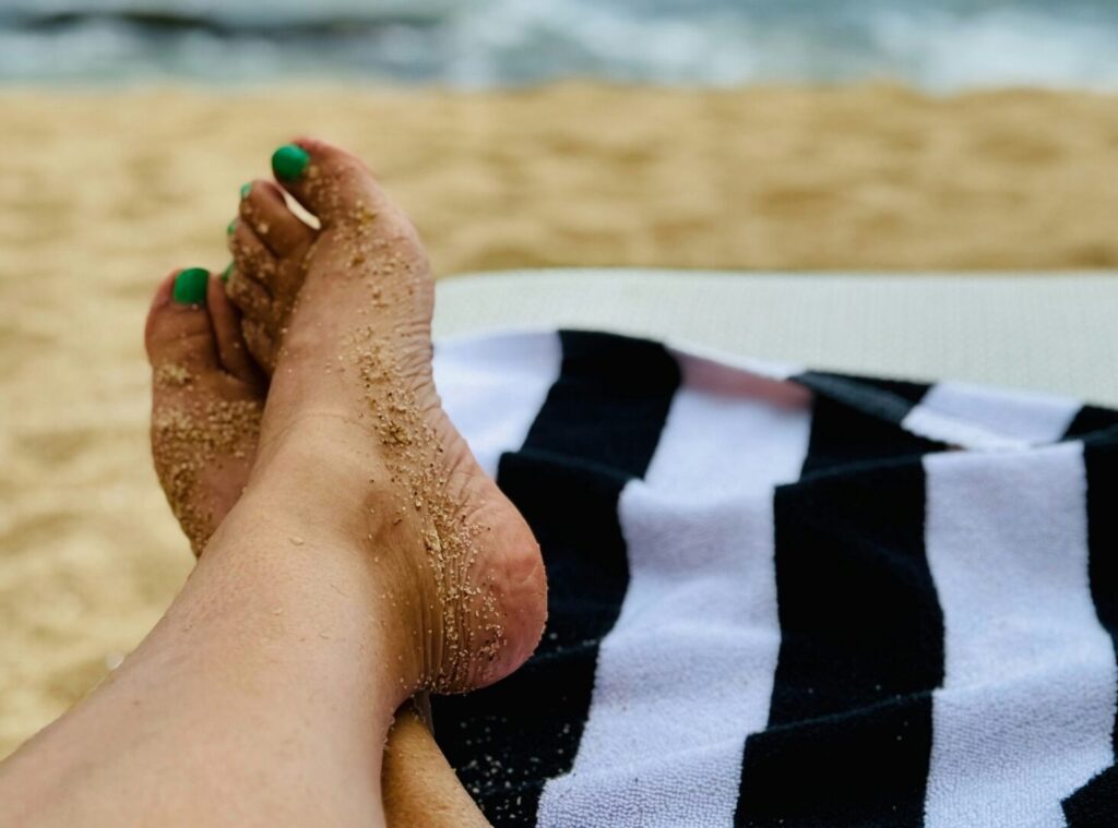 Blauw gelakte teennagels boven een zwart-wit gestreepte handdoek aan het strand
